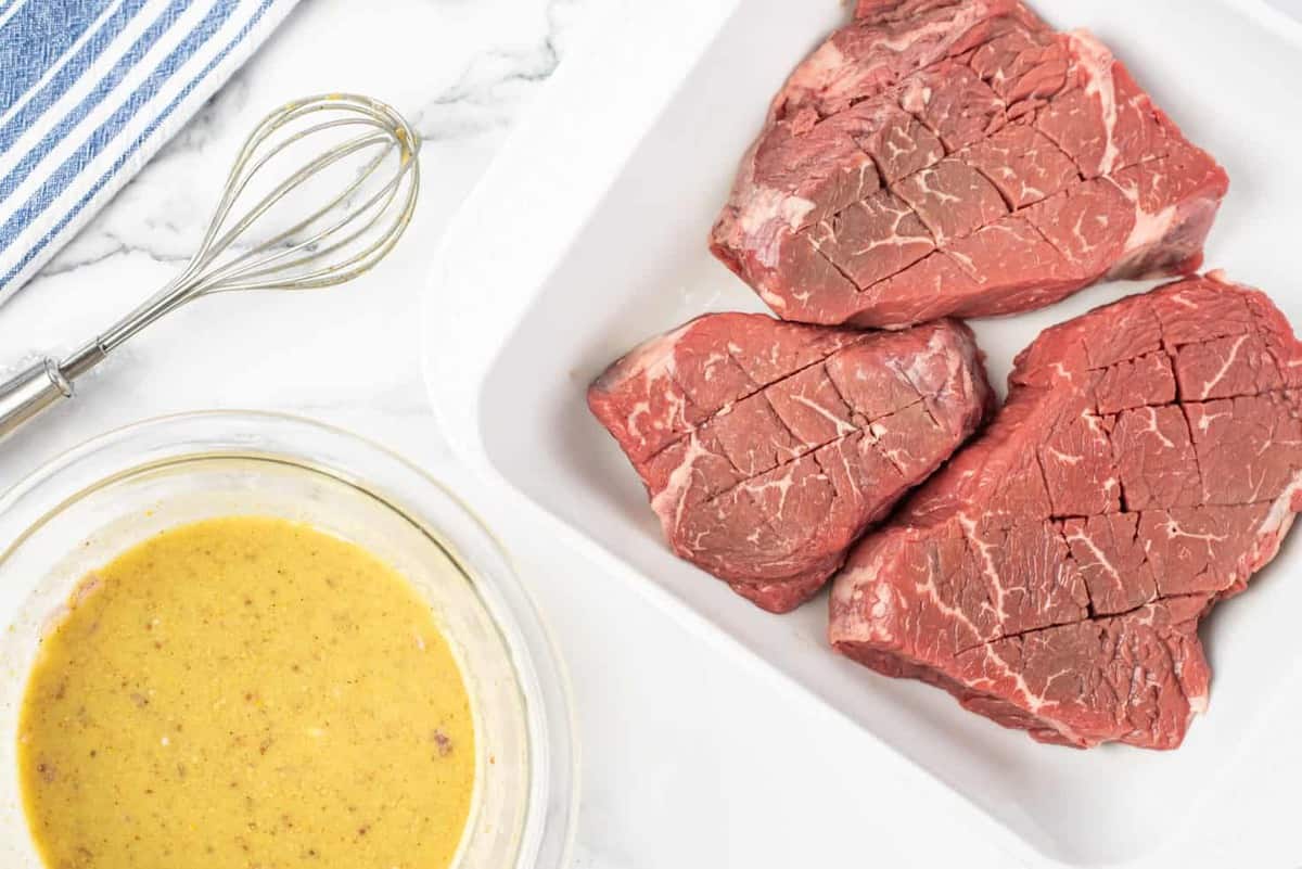 A dish with raw steak, bowl of steak marinade recipe to the side.