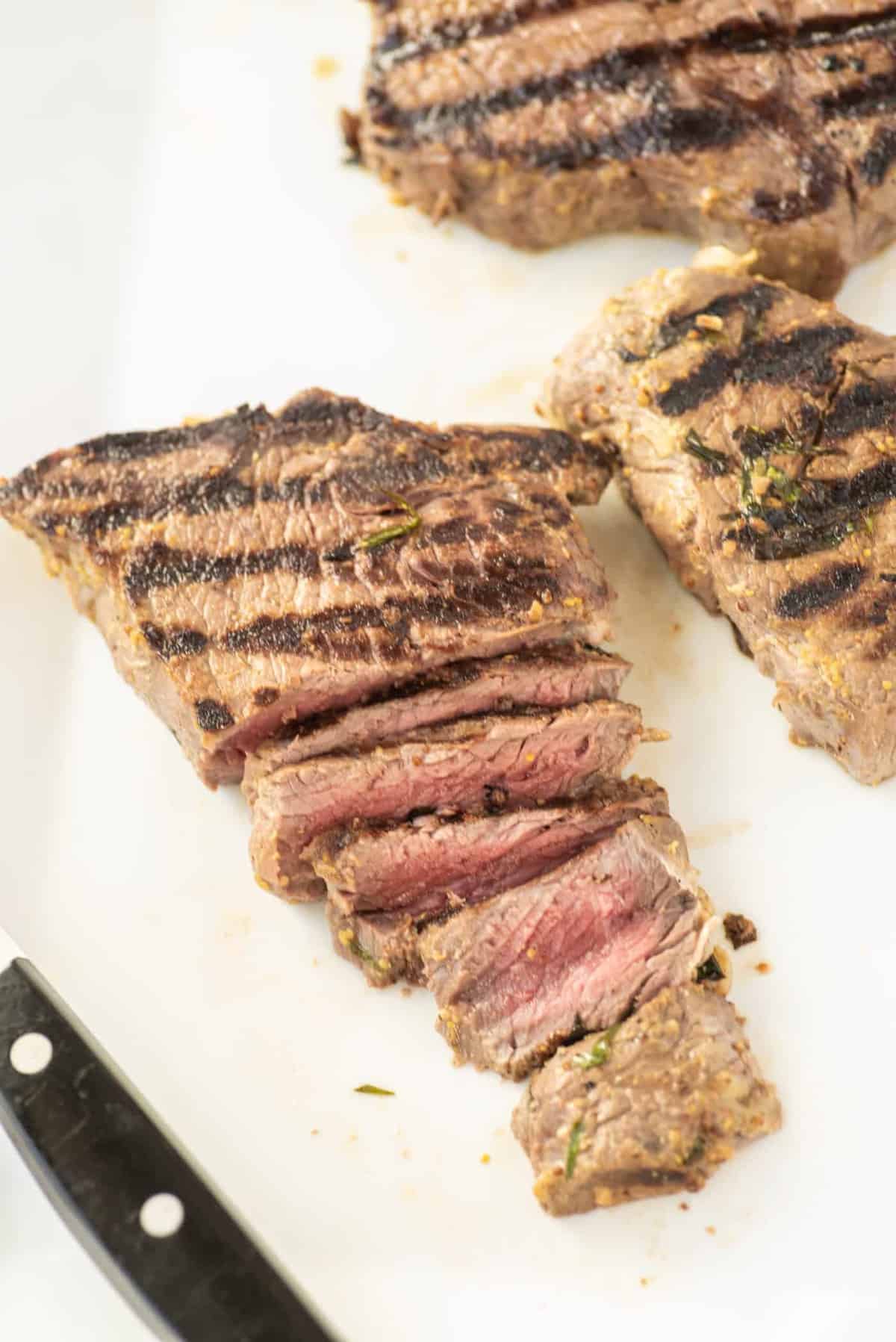 Marinated steak on a white plate, one sliced. 