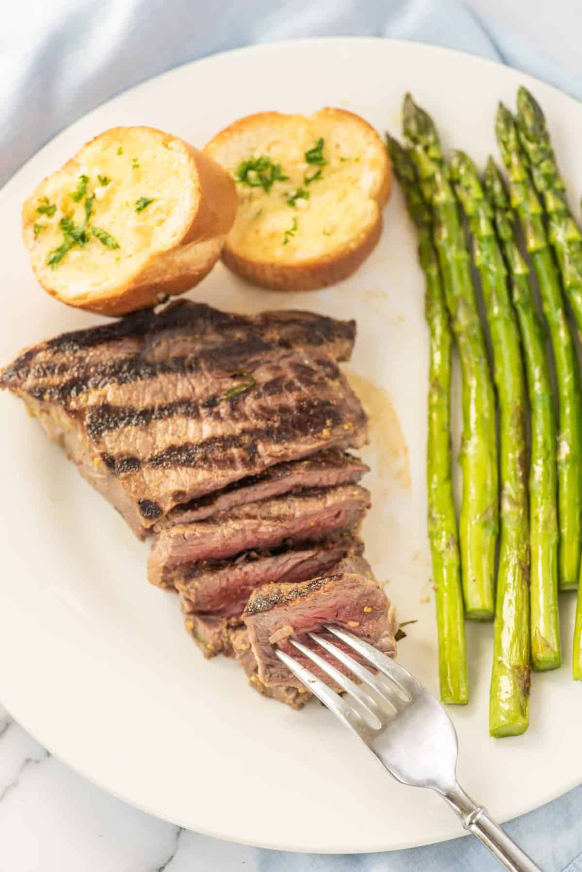 A grilled steak with a side of asparagus on a white plate.