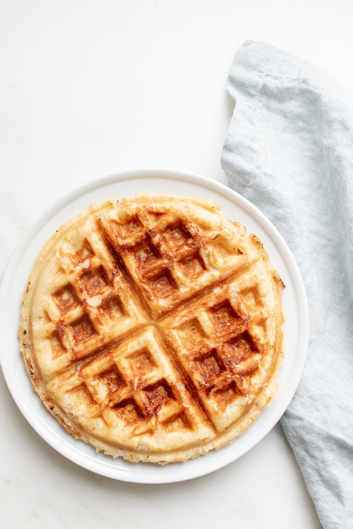 An authentic Belgian waffle on a white plate, with a blue linen towel behind it.