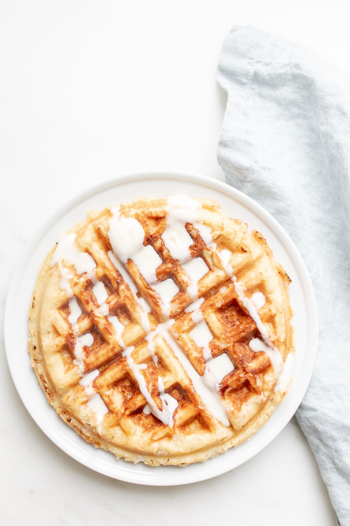 An authentic Belgian waffle on a white plate, with a blue linen towel behind it.