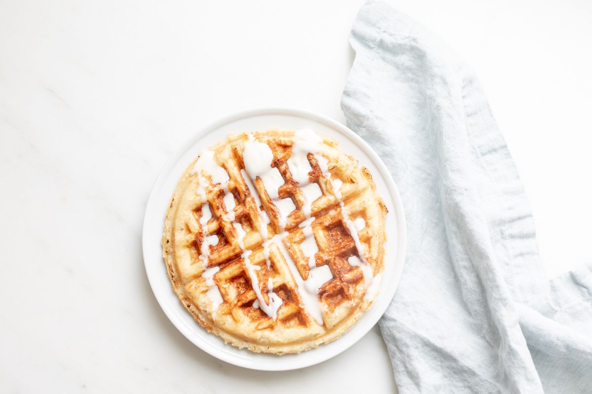 An authentic Belgian waffle on a white plate, with a blue linen towel behind it.