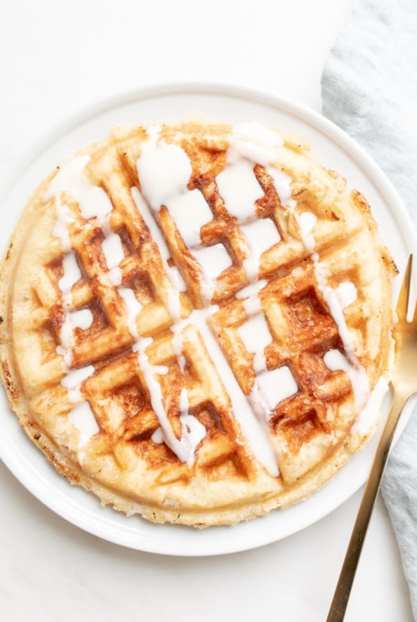 An authentic Belgian waffle on a white plate, with a blue linen towel behind it.