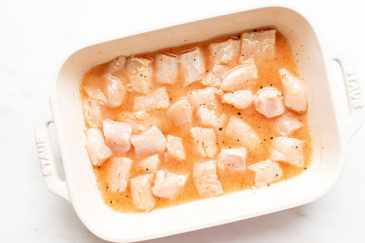 chicken kabob marinade with chunks of uncooked chicken in a white baking dish