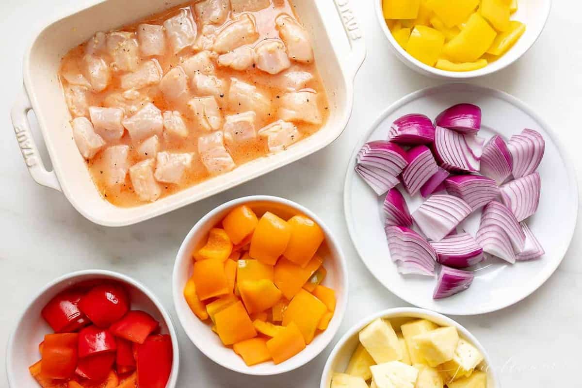 Kabob ingredients in white dishes on a marble countertop. 
