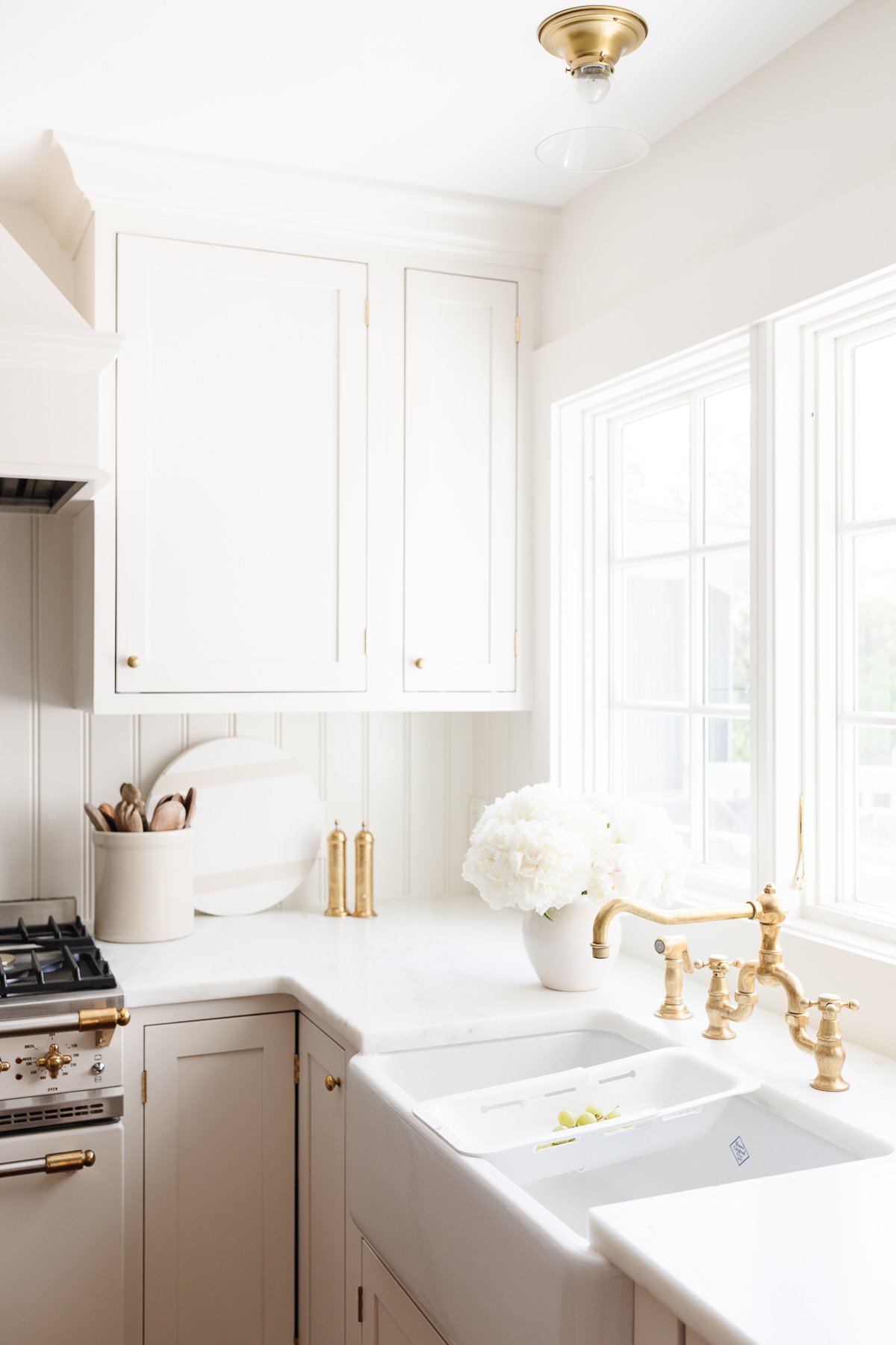 A cream kitchen with brass hardware, a farm sink and Danby marble countertops.