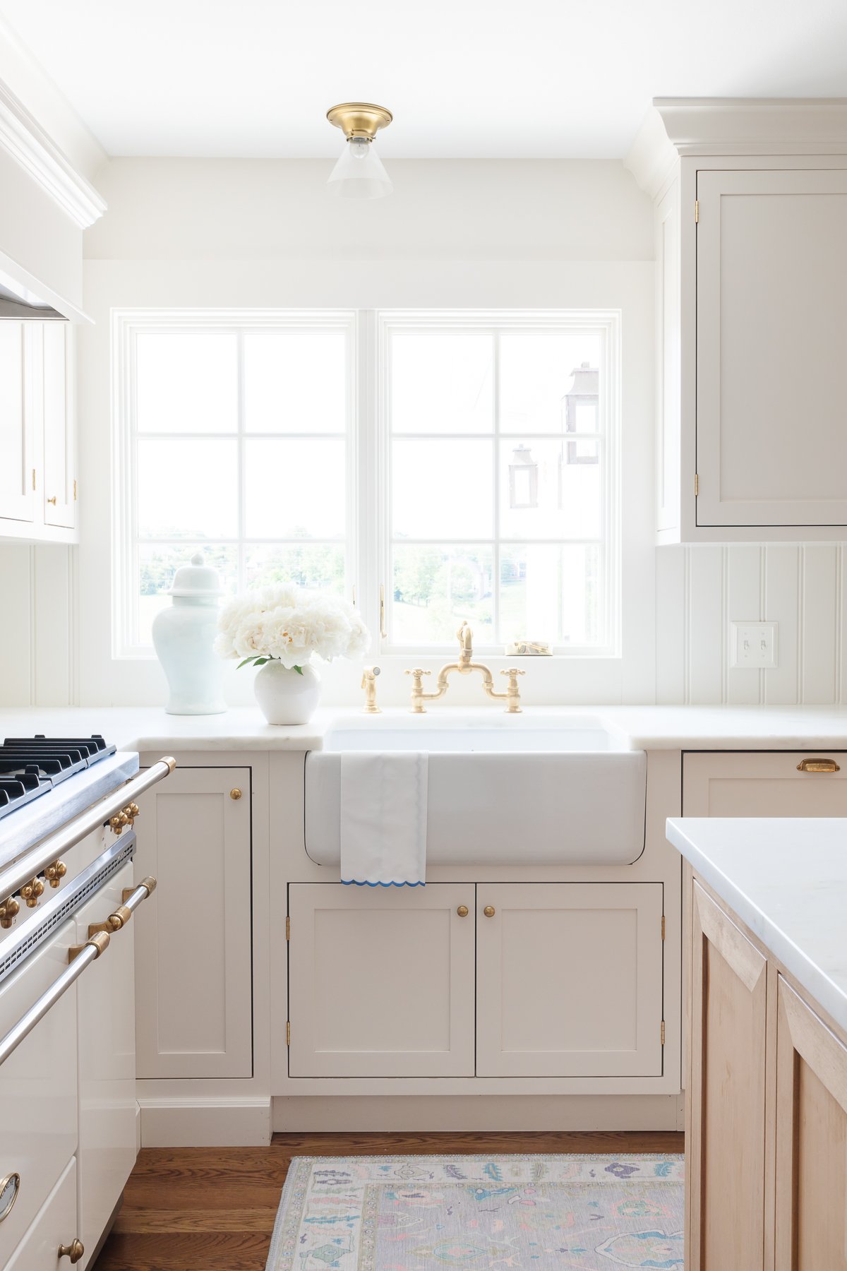 A cream kitchen with brass hardware, a farm sink and Danby marble countertops.