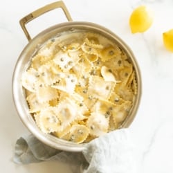 A stainless steel pan filled with ravioli in a white wine lemon caper sauce.