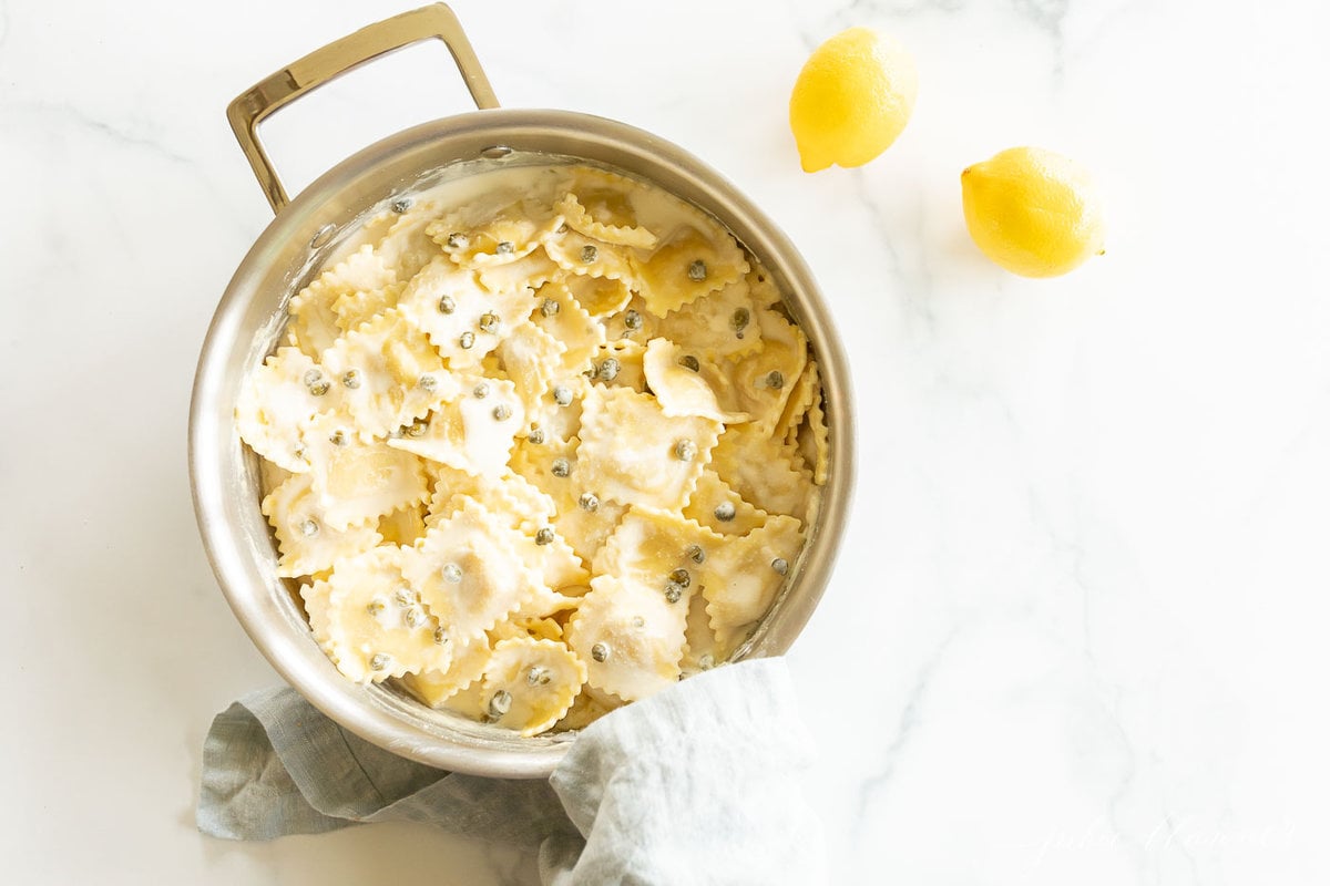 A stainless steel pan filled with ravioli in a white wine lemon caper sauce. 