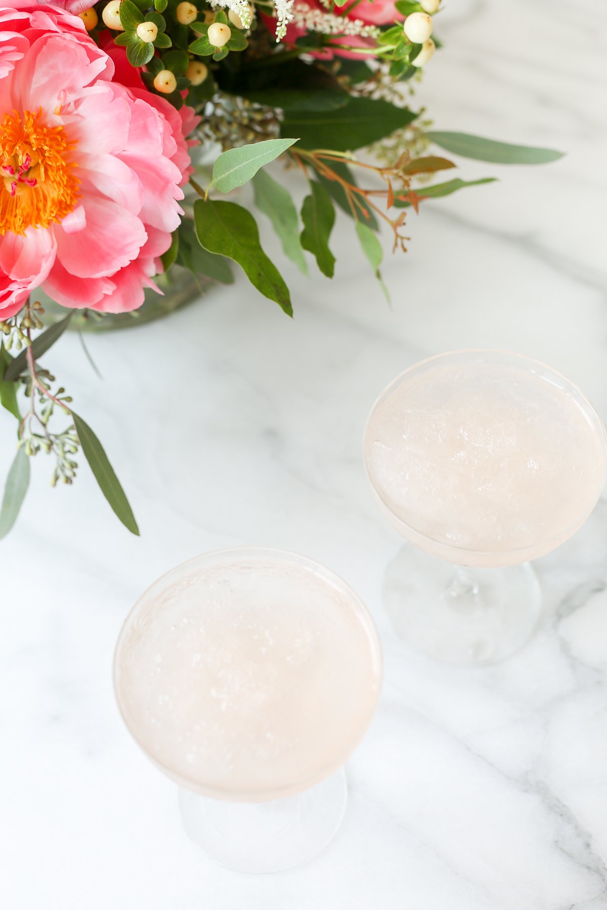 Two glasses of frosé on a marble table next to a bouquet of flowers.