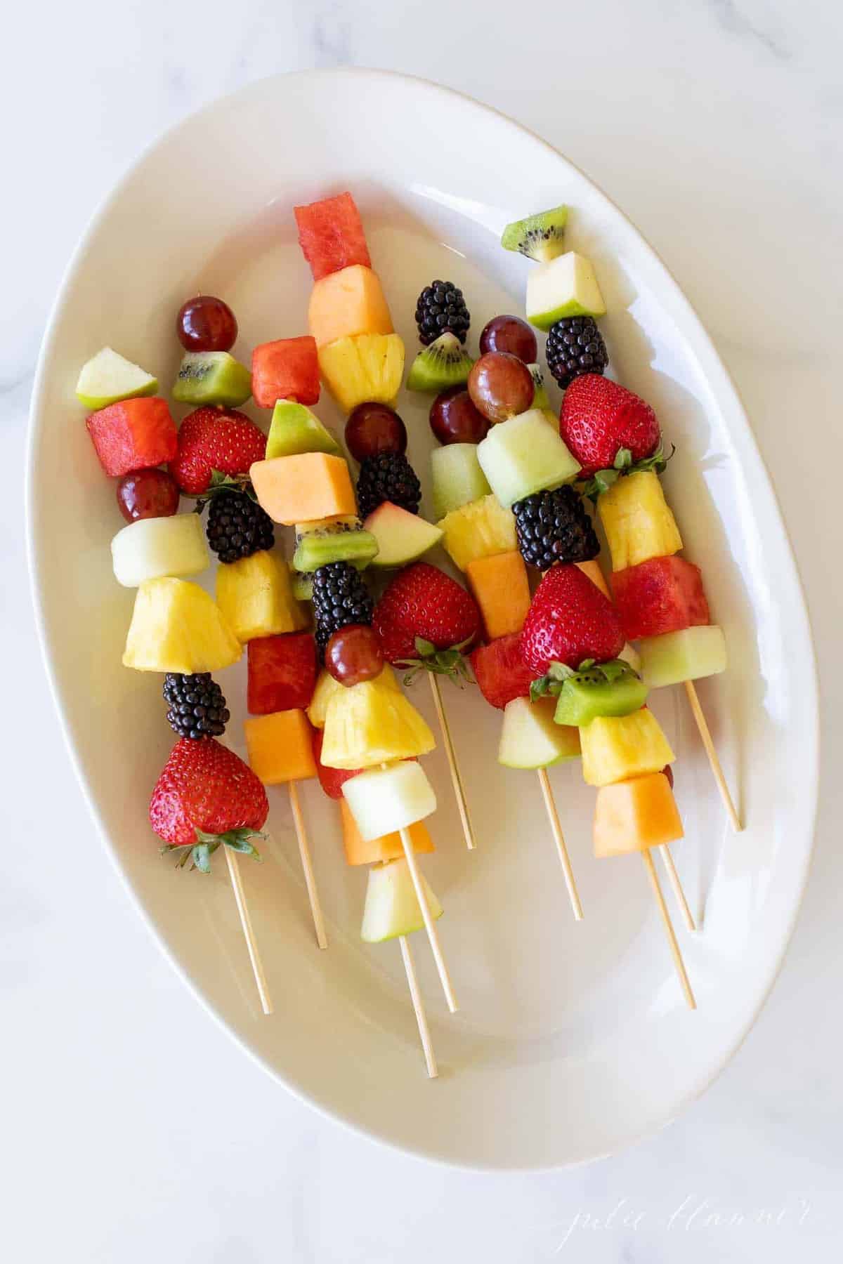 Colorful fruit skewers on a white oval platter.