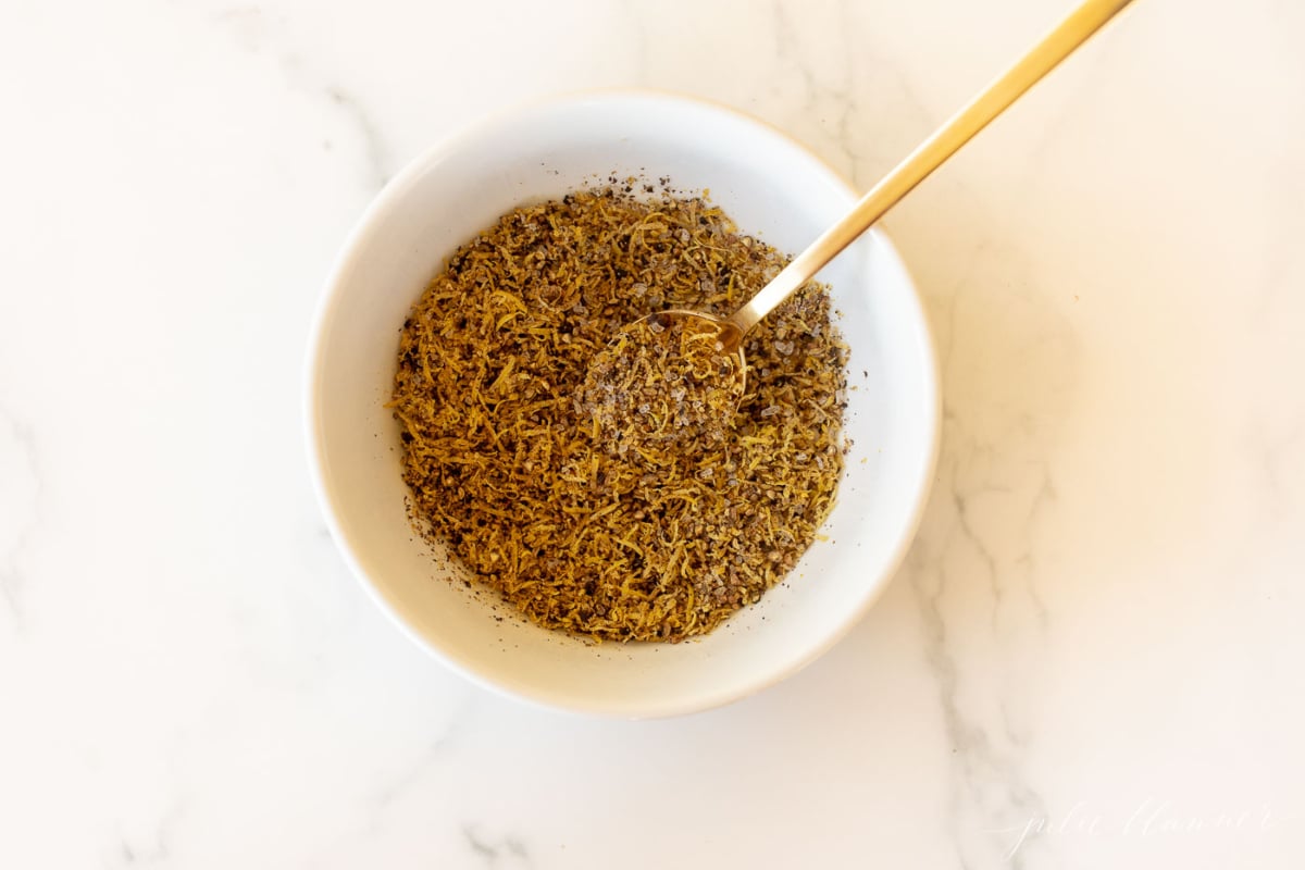 A white bowl on a marble surface, filled with lemon pepper seasoning blend.