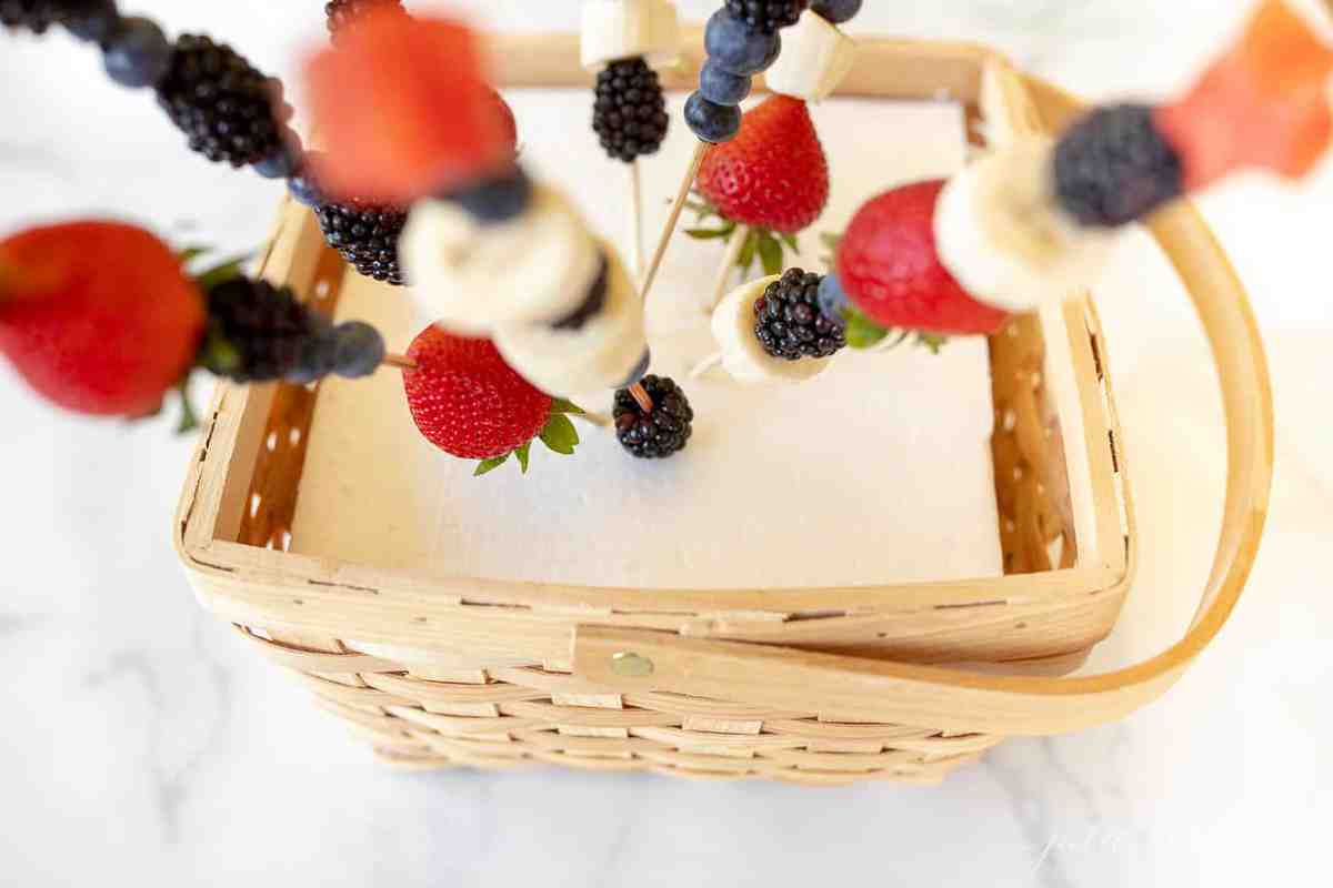 A marble surface with a wooden basket, sheet of white foam inside, fruit skewers shooting out.