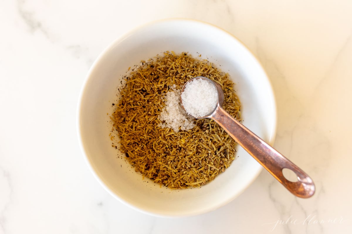 A white bowl on a marble surface, filled with lemon pepper seasoning blend.