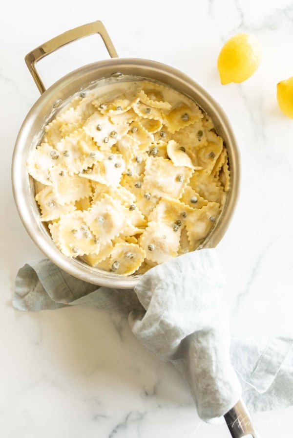 A stainless steel pan filled with ravioli in a white wine lemon caper sauce.