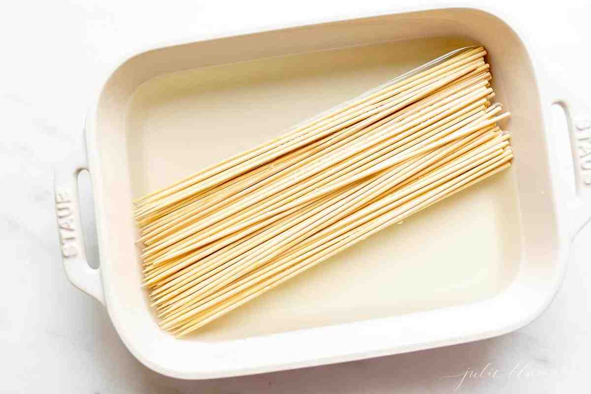 A white dish filled with water and bamboo skewers for future shrimp kabobs.