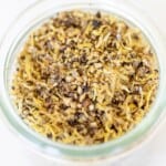 A glass jar on a marble surface, filled with lemon pepper seasoning blend.