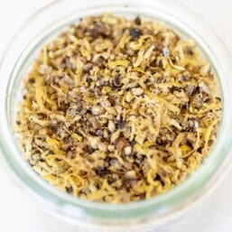 A glass jar on a marble surface, filled with lemon pepper seasoning blend.