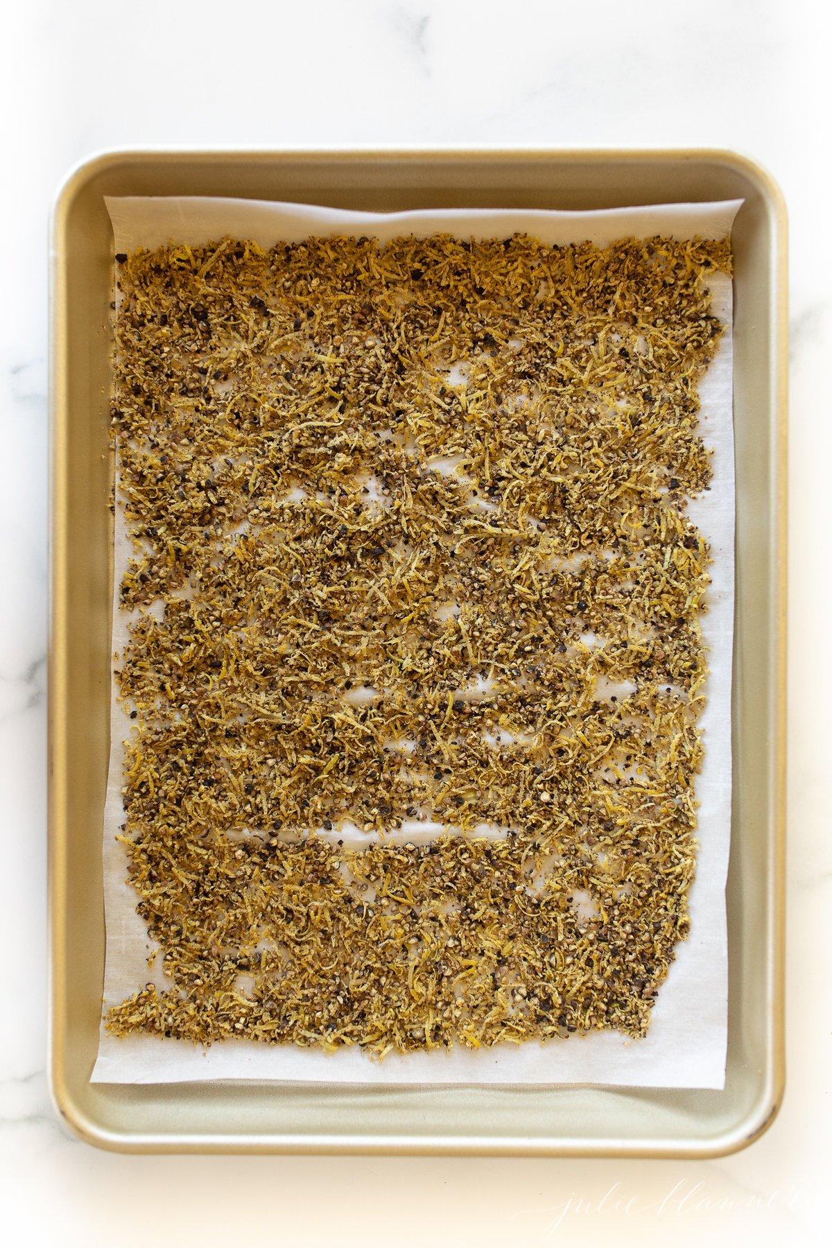 Homemade lemon pepper seasoning on a gold baking sheet.