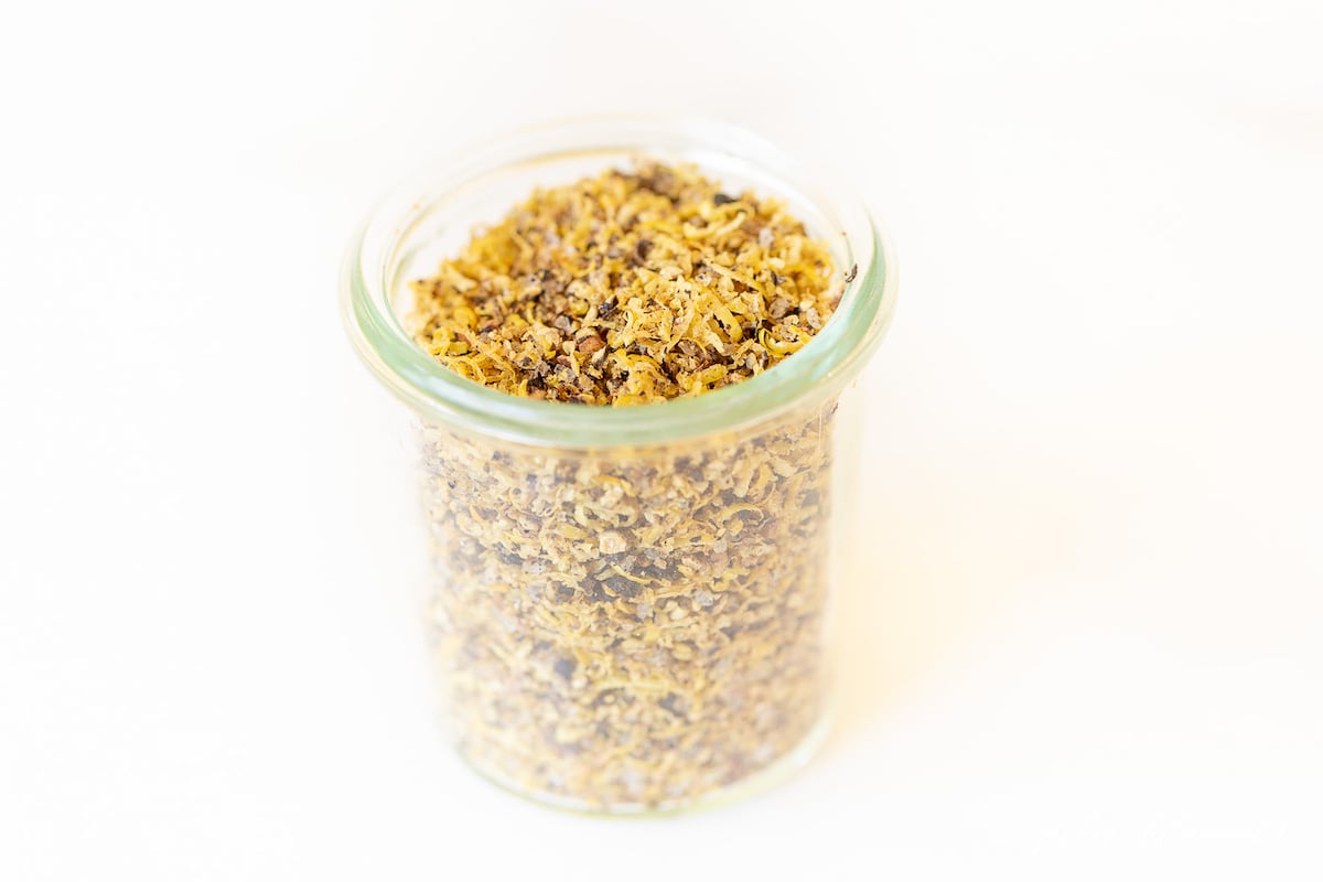 A glass jar on a marble surface, filled with lemon pepper seasoning blend.