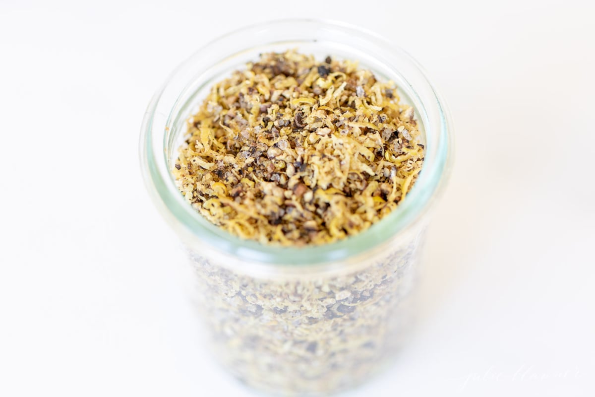 A glass jar on a marble surface, filled with lemon pepper seasoning blend.