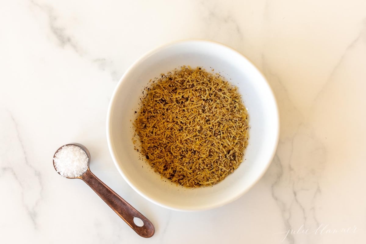 A white bowl on a marble surface, filled with lemon pepper seasoning blend.