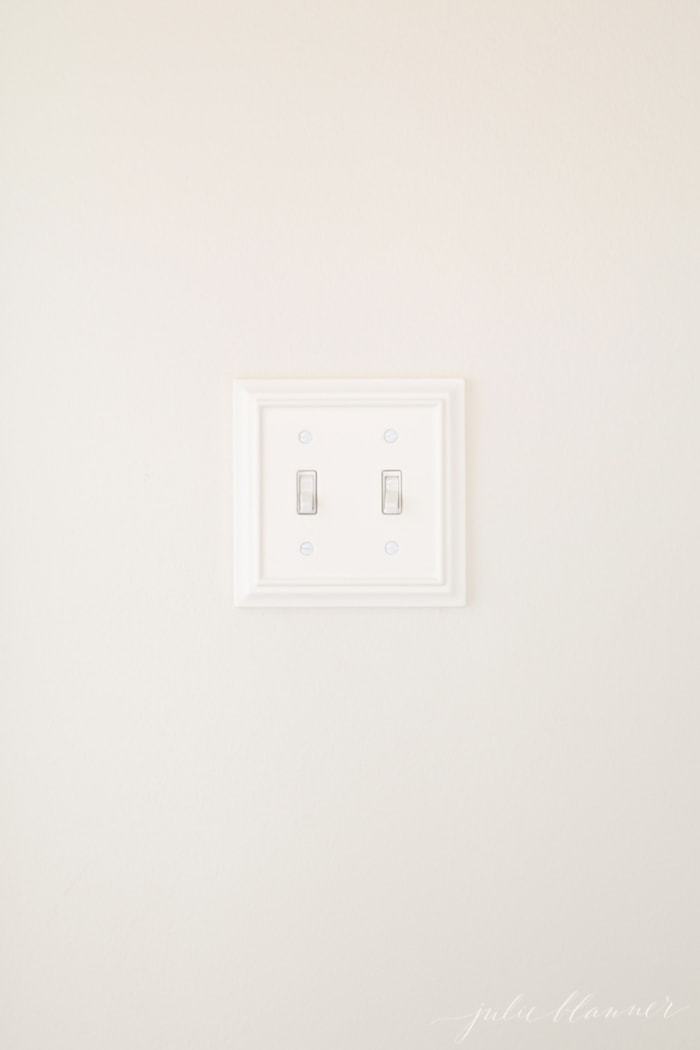 A cream painted wall with a pretty white wooden double light switchplate