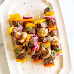 A white platter filled with grilled steak kabobs.