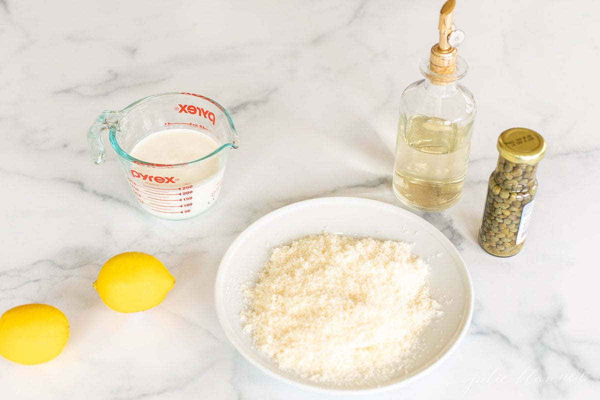 Ingredients for a white wine lemon caper sauce on a marble countertop.