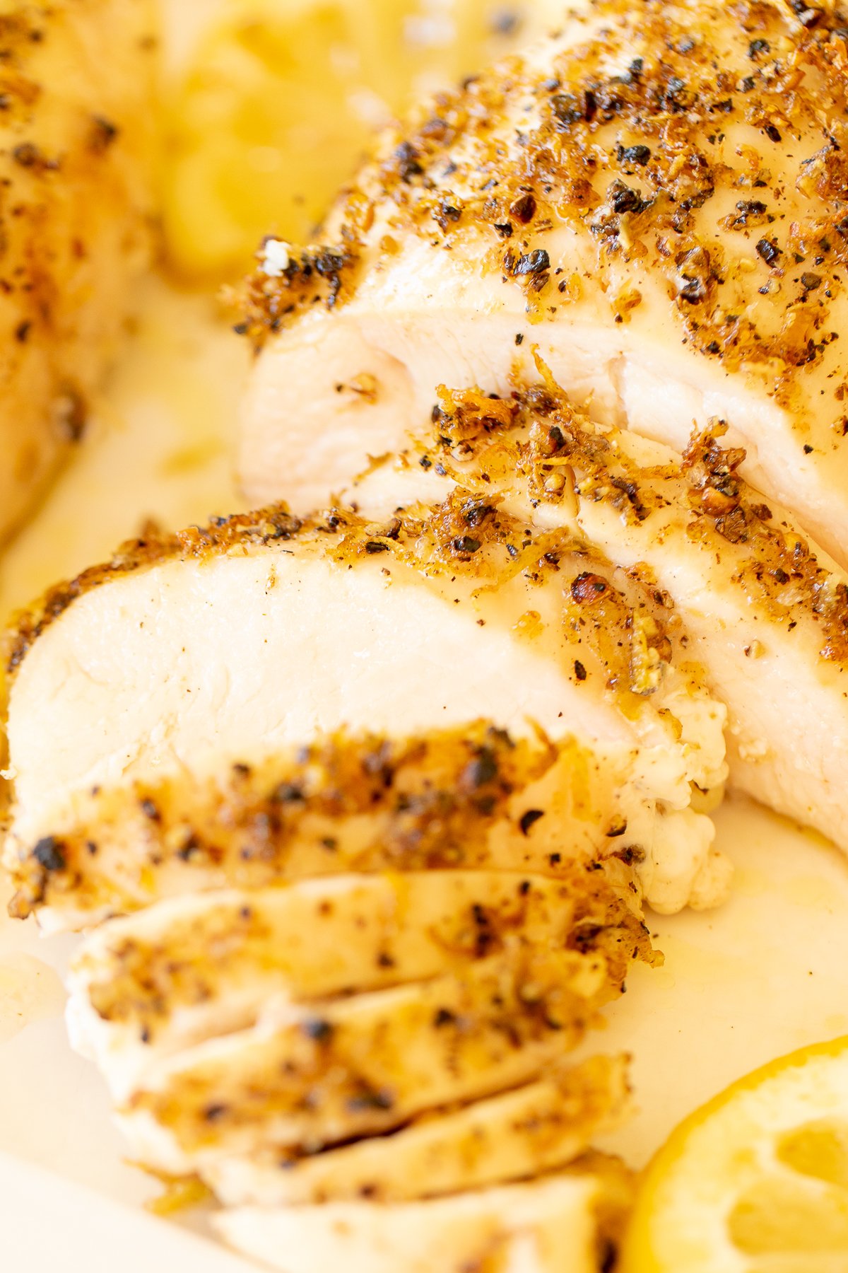 A sliced lemon pepper chicken breast on a white serving platter.
