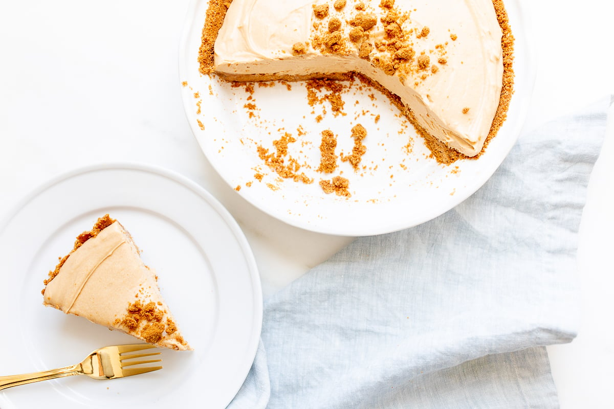 A slice of no bake cookie butter cheesecake on a white plate, with a pie pan behind it.