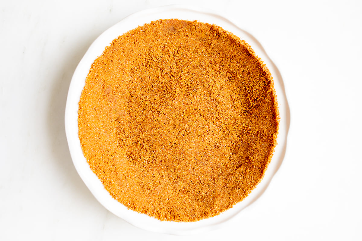 A white pie pan full of speculoos cookie crust for a pie.