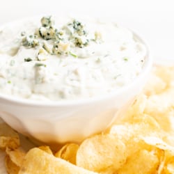 blue cheese dip in a white bowl, on a platter of potato chips.