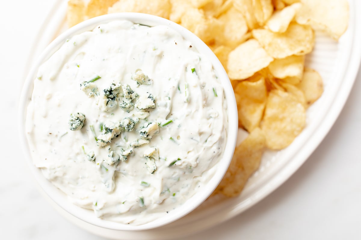 blue cheese dip in a white bowl, on a platter of potato chips.