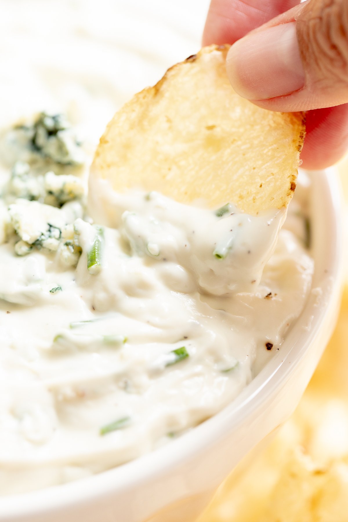 blue cheese dip in a white bowl, with fingers gripping a chip to dip into it.