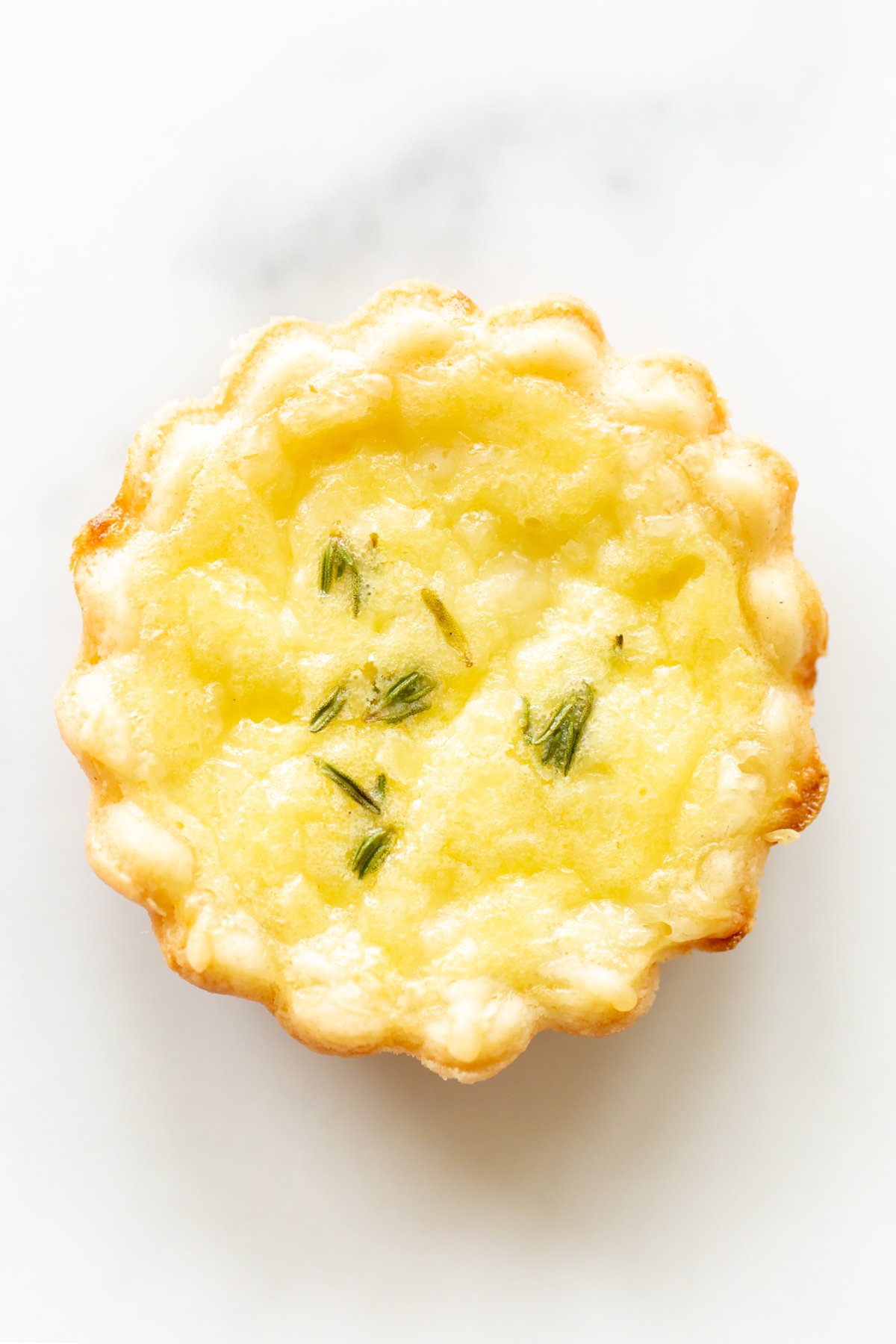 A single mini cheese tart on a marble countertop.