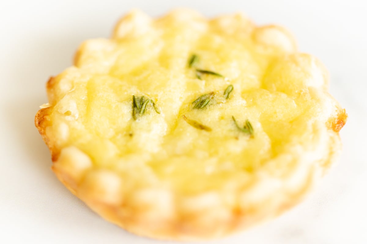 A single mini cheese tart on a marble countertop.