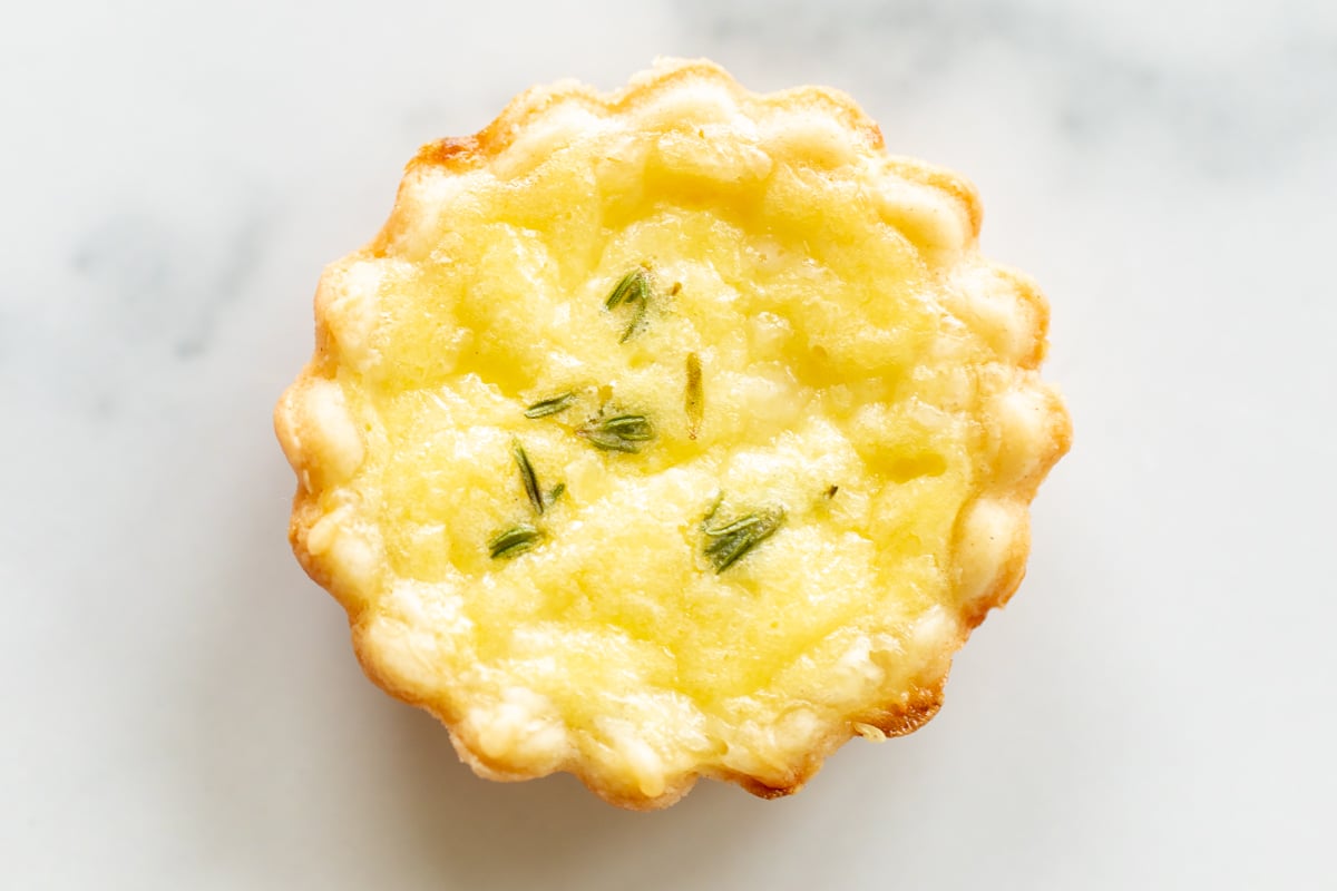 A single mini cheese tart on a marble countertop.