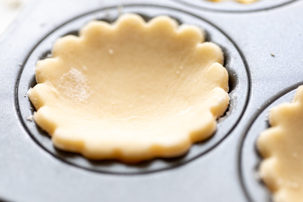 an unbaked cream cheese pie crust cut into a round shape for mini cheese tarts.