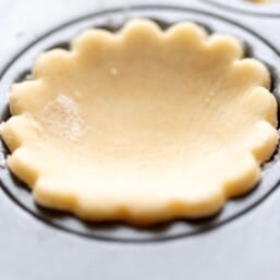 A scalloped cream cheese pie crust cut out, resting in a muffin tin.