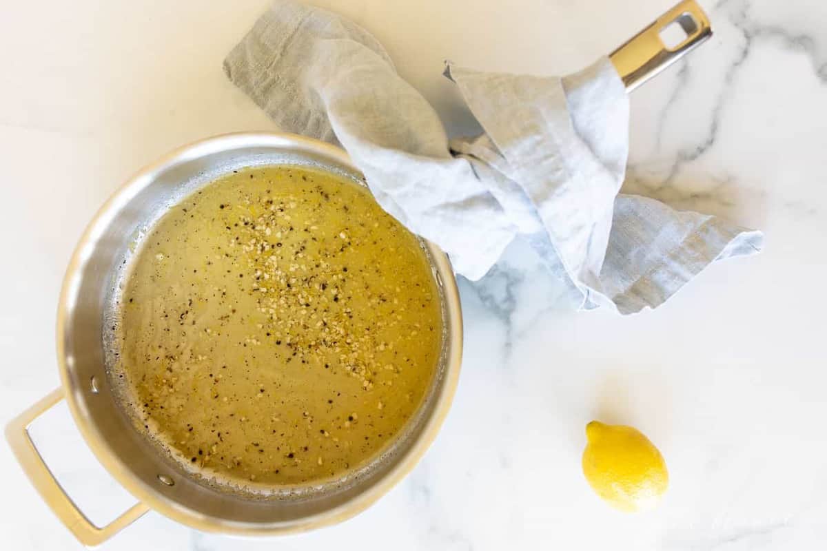 A saucepan on a marble surface, lemon pepper sauce inside.