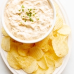 A bowl full of homemade french onion dip, surrounded by potato chips.