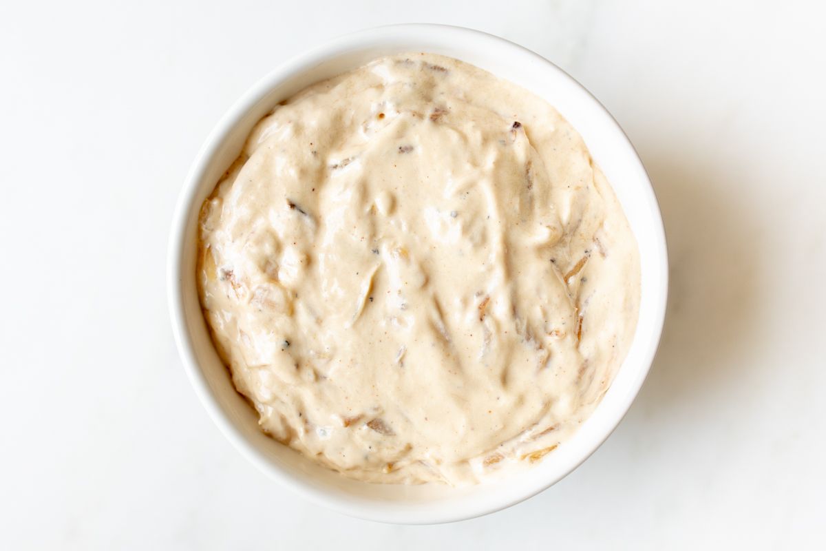 A white bowl full of French onion dip made with caramelized onions.