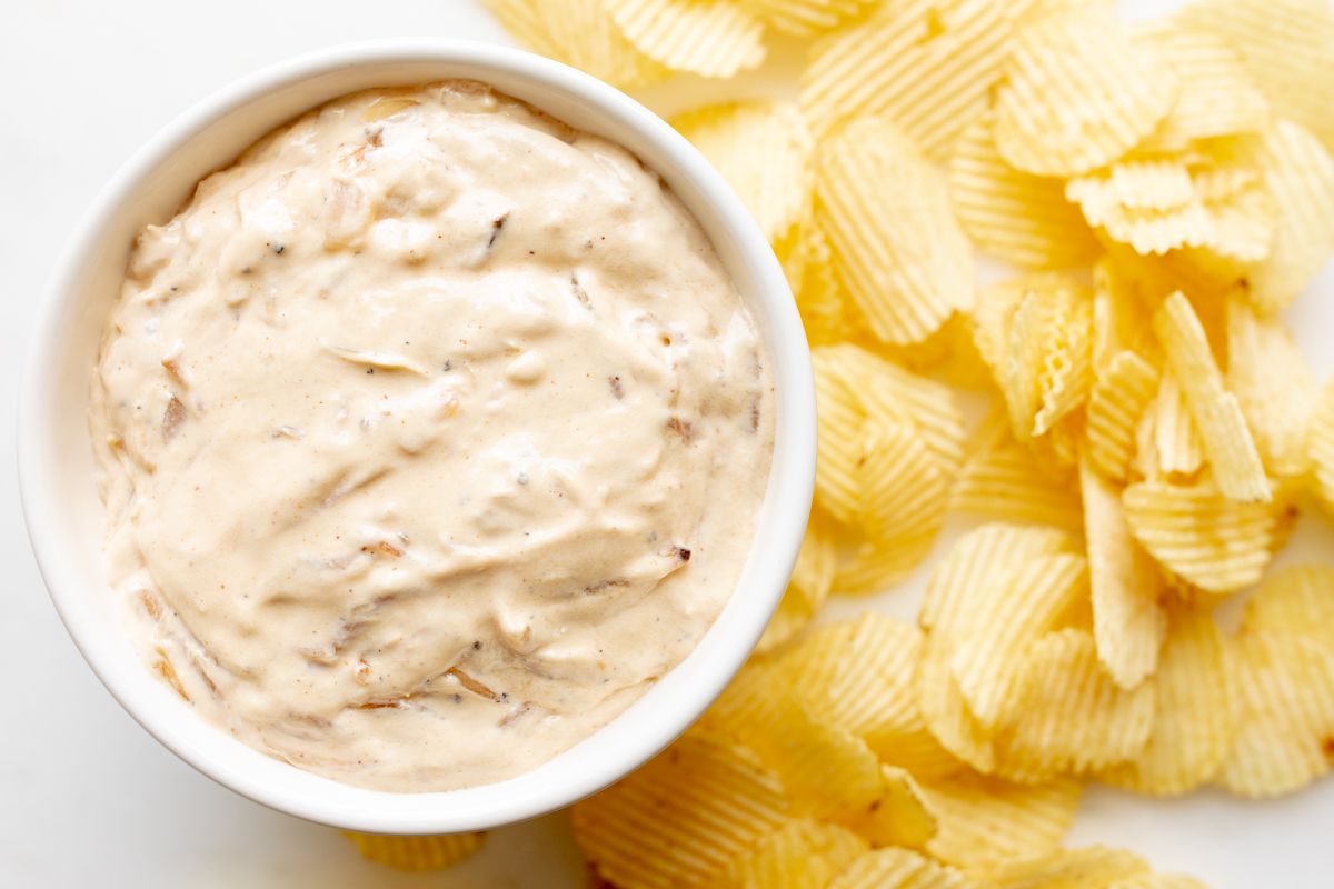 A bowl full of homemade french onion dip, surrounded by potato chips. 