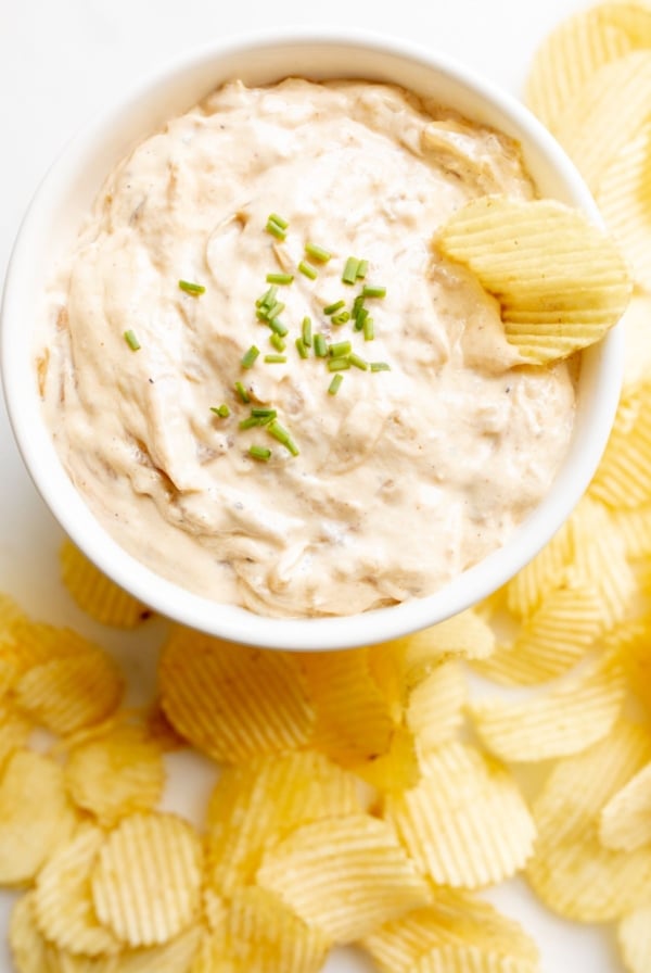 A bowl full of homemade french onion dip, surrounded by potato chips.