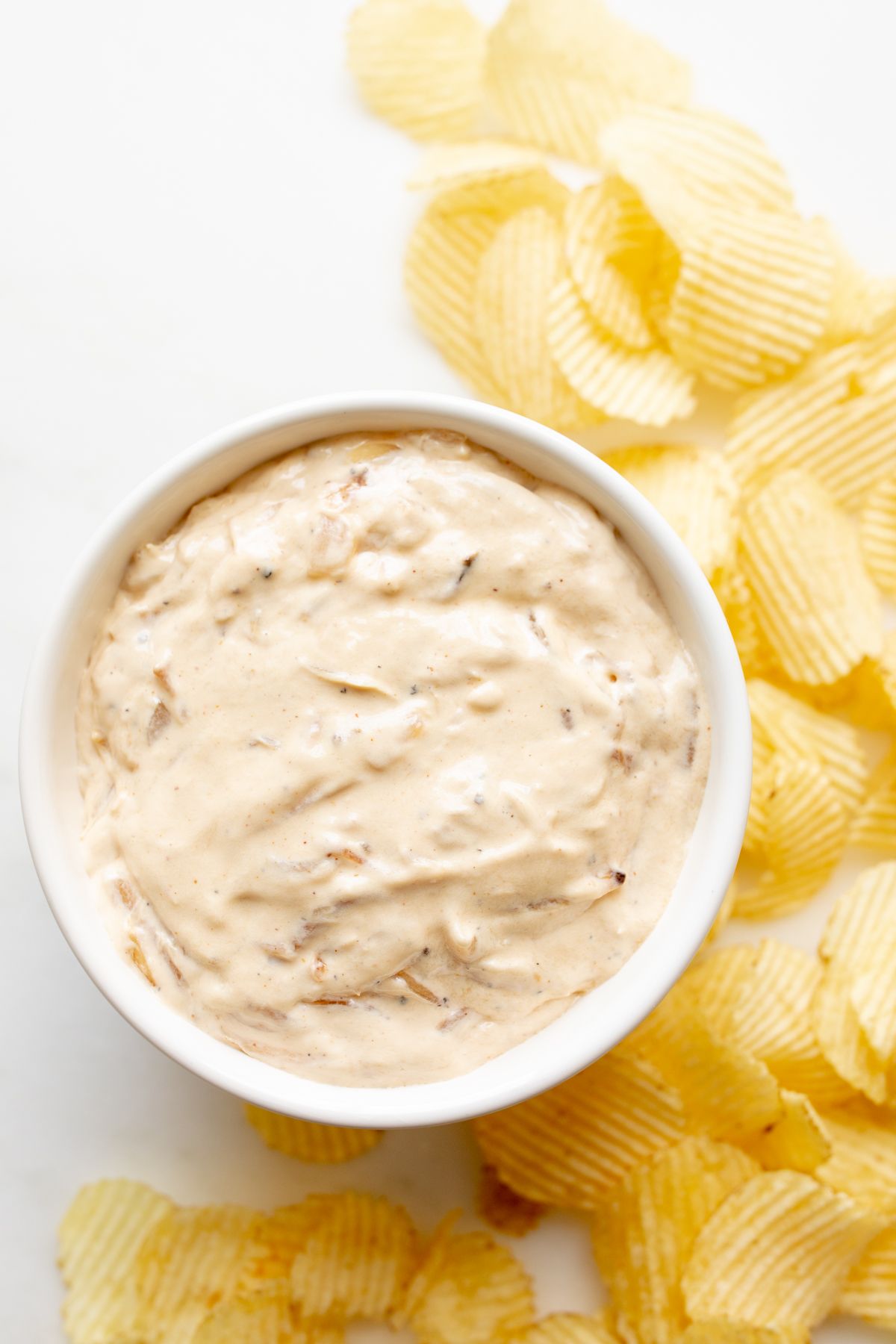 A bowl full of homemade french onion dip, surrounded by potato chips.