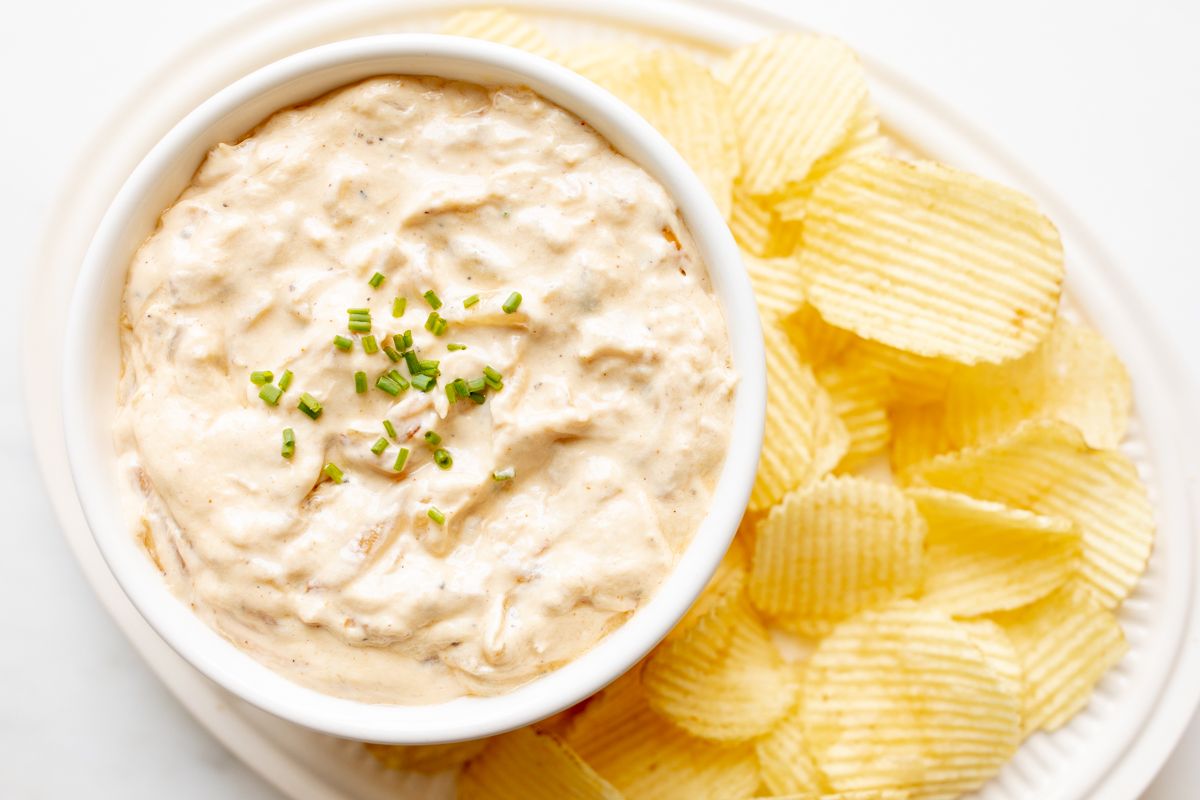 A bowl full of homemade french onion dip, surrounded by potato chips.