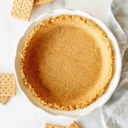graham cracker pie crust in white pie dish with graham crackers surrounding it