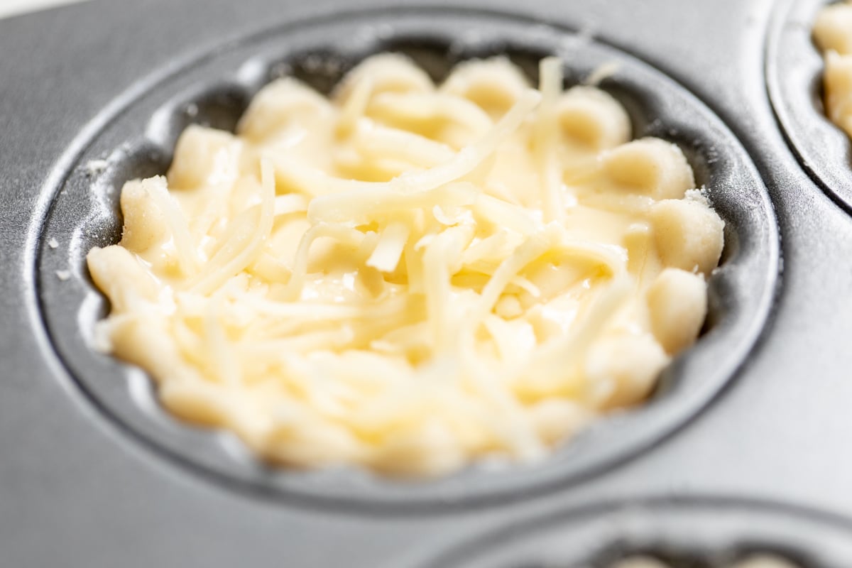 A mini cheese tart crust inside a muffin tin, prior to baking.