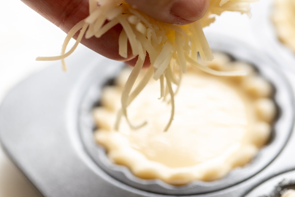 A mini cheese tart crust inside a muffin tin, prior to baking.